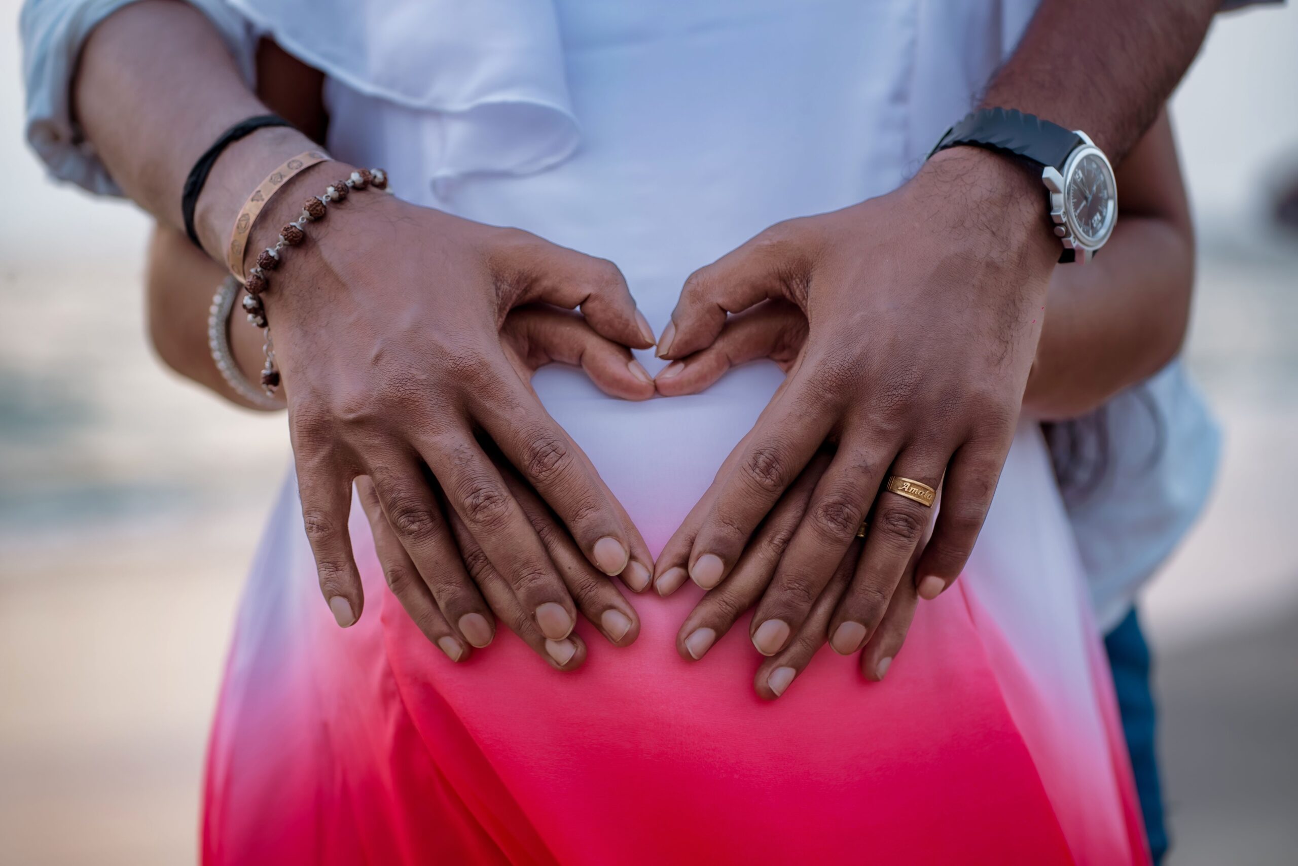 Expectant couple forms a heart with hands over pregnant belly, symbolizing love and anticipation.