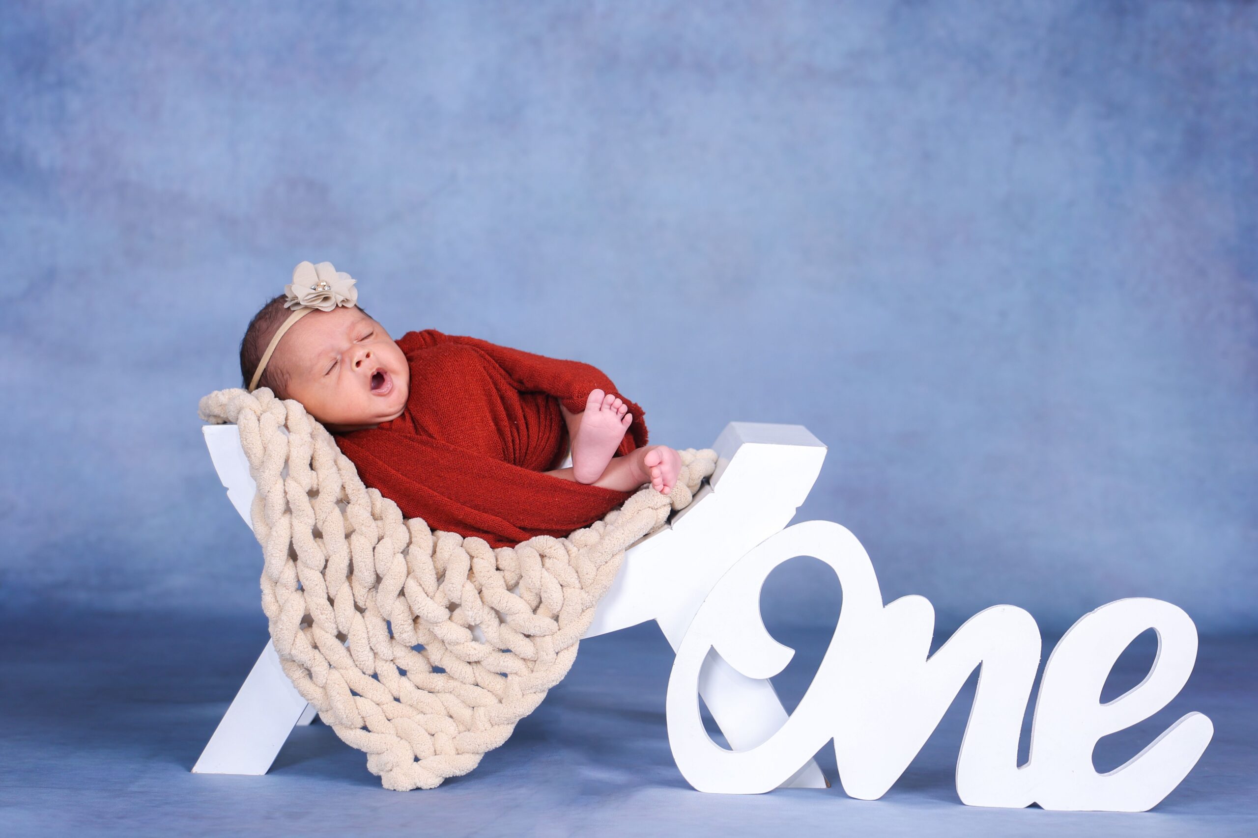 Cute newborn in a red outfit on 'One' prop, perfect for first birthday photoshoot.