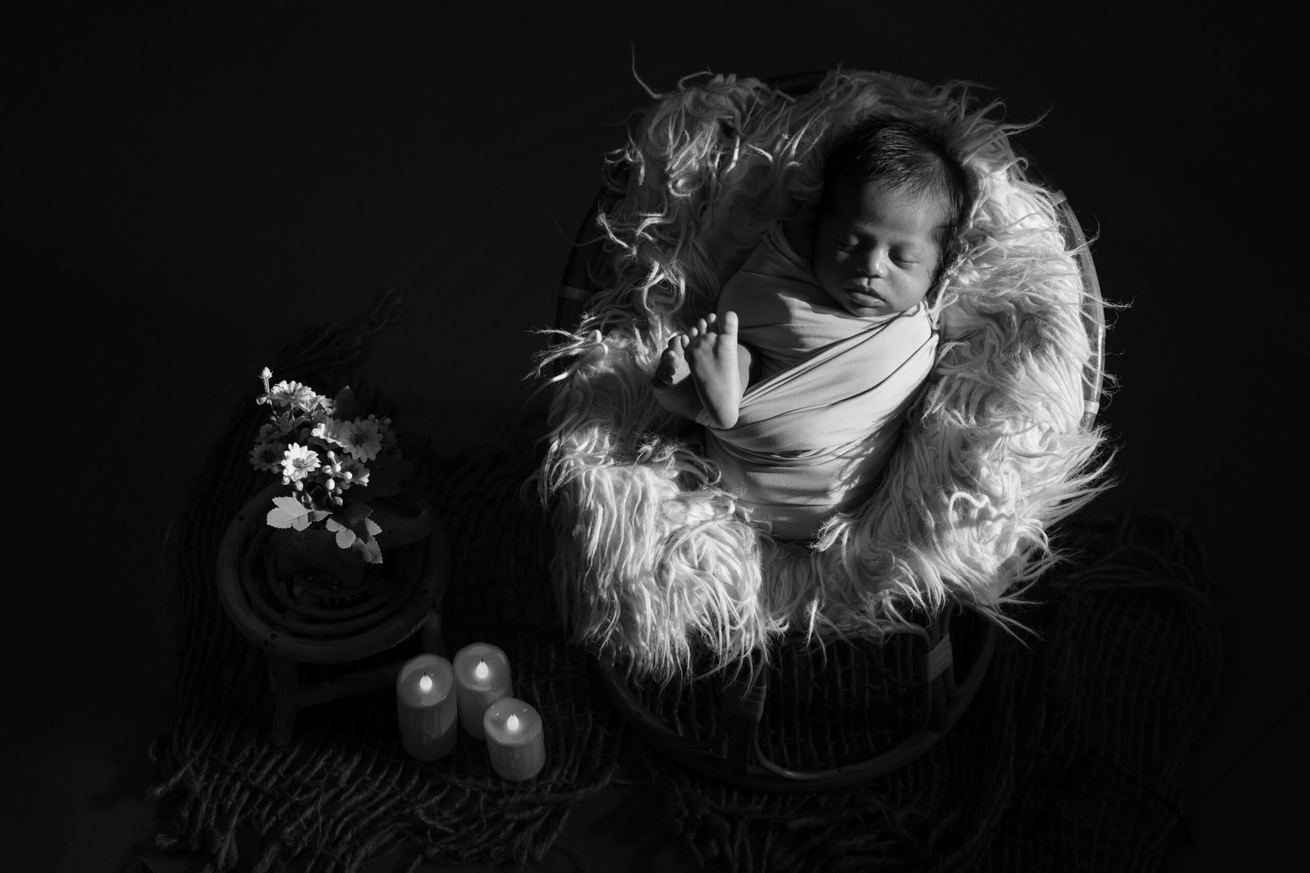 Tender black and white portrait of a newborn baby wrapped in a blanket, surrounded by soft lighting and decor.
